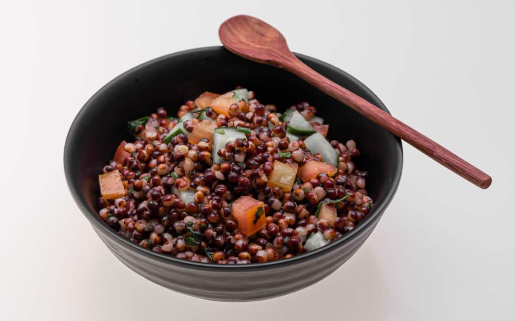 Bowl with sorghum, tomato and cucumber and spoon on top