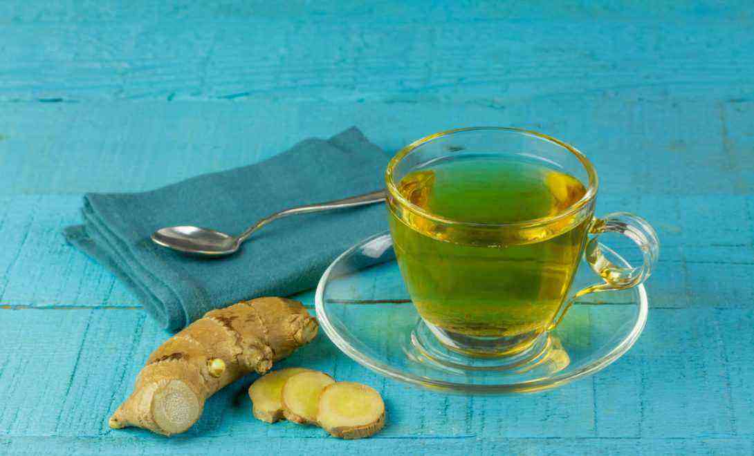 Ginger tea in a glass cup next to whole and sliced ​​ginger on blue wooden table